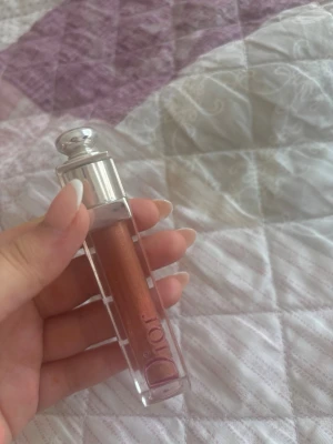 Dior läppglans i persikoton - Säljer ett lyxigt läppglans från Dior i en snygg persikoton med skimrande finish. Förpackningen är genomskinlig med silverfärgat lock och Dior-logga på sidan. Perfekt för dig som vill ha glansiga och fylliga läppar med en hint av färg. den har använt några gånger. Det finns 80 % av produkten kvar
