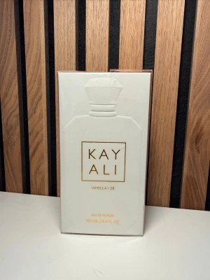 Kayali Vanilla | 28 Eau de Parfum - Helt ny Kayali Vanilla | 28 Eau de Parfum är en lyxig parfym i en elegant vit förpackning med guldtext. Doften har noter av vaniljorkidé, tonkaböna, brunt socker, amberträ och mysk. Flaskan rymmer 100 ml och har en modern, stilren design som känns exklusiv.