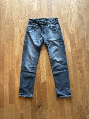Grå raka jeans med tvättad look - Snygga grå jeans med tvättad finish och raka ben. Klassisk femficksmodell med bälteshällor och knappgylf. Perfekta för en avslappnad och trendig stil. Materialet är denim i bomull. Modellen är Tapered/Mike