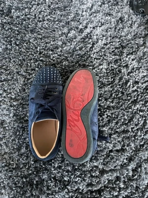 Blåa Louboutin sneakers med nitar - Säljer ett par mörkblå sneakers från Christian Louboutin i mocka med ikoniska röda sulor och coola nitar på tån. Skorna har matchande blå skosnören och en låg profil som ger en clean look