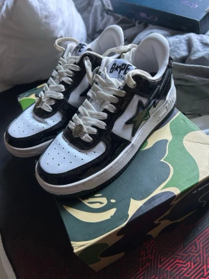 BAPE STA svarta och vita sneakers - Säljer ett par BAPE STA sneakers i svart och vitt med glansiga paneler och den ikoniska stjärnan på sidan. Skorna har vita snören, perforerad tåbox och klassisk BAPE-logga på hälen. Kommer med originalkartong i camomönster. PRIS KAN DISKUTERAS 