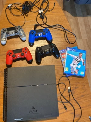 PlayStation 4 med fyra handkontroller - PlayStation 4 spelkonsol i svart med fyra DualShock 4-handkontroller i färgerna svart, röd, blå och transparent. Medföljer kablar och två PS4-spel, bland annat FIFA 19 och LEGO-spel. Perfekt för gamingkvällar med vänner. Funkar jätte fint inge stick drift av vad jag vet