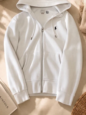 Vit hoodie från Polo Ralph Lauren - Snygg vit hoodie från Polo Ralph Lauren med dragkedja, huva med dragsko och klassisk svart logga på bröstet. Mjuk bomullskänsla och två fickor framtill. Perfekt för en chill och stilren look.