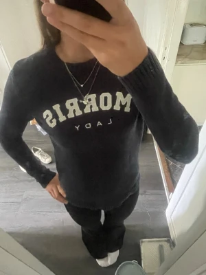 Mörkblå stickad tröja Morris Lady - Snygg mörkblå stickad tröja från Morris Lady med vit text framtill. Tröjan har rund halsringning och ribbade muddar vid ärmslut och nederkant. Perfekt till jeans eller kjol för en klassisk look.