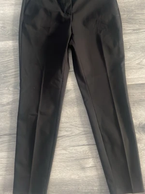 Svarta raka kostymbyxor - Snygga svarta kostymbyxor med rak passform och pressveck. Byxorna har en klassisk midja och är tillverkade i ett slätt tyg som ger en stilren look. Perfekta för dig som vill ha en clean och tidlös stil. 38 midjan, 30 längd