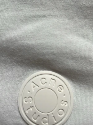 Vit t-shirt från Acne Studios - Klassisk vit t-shirt från Acne Studios med rund hals och korta ärmar. T-shirten har en diskret patch med Acne Studios-loggan på bröstet. Tillverkad i mjuk bomull för en skön och avslappnad känsla.
