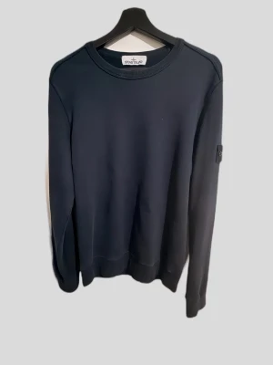Mörkblå sweatshirt från Stone Island - Snygg mörkblå sweatshirt från Stone Island med klassisk rund halsringning och ikonisk logopatch på ärmen. Tröjan har en enkel och stilren design, perfekt för en avslappnad streetwear-look. Tillverkad i mjukt bomullsmaterial och har långa ärmar.
