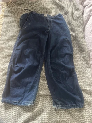 Blå loose fit jeans med snörning - Säljer ett par mörkblå jeans med loose fit och snörning i midjan och vid bensluten. Jeansen har en avslappnad passform och praktiska fickor fram. Perfekta för en chill och bekväm stil.