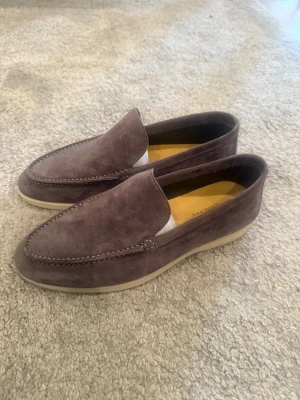 Loro piana summerwalk - Snygga loafers i grå mocka med stilren design och kontrasterande vit sula. Skorna har klassisk form med diskreta sömmar och är perfekta för en avslappnad men ändå uppklädd look. Passar till jeans eller chinos för en trendig stil. Box och papper finns tillgängliga 