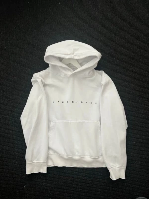 Vit hoodie från Jack & Jones - Snygg vit hoodie från Jack & Jones med minimalistisk logga tryckt på bröstet. Klassisk känguruficka framtill och huva. Tillverkad i mjukt material som passar perfekt för en avslappnad stil.