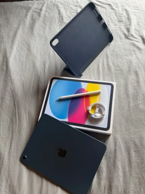iPad (A16) 11" – 128GB Wi-Fi (Blue) + Skal, Penna & Garanti kvar! - Säljer en iPad (A16) 11" Wi-Fi 128GB i snygg blå färg, i princip nyskick och sparsamt använd. Skärmen och baksidan är i toppskick, batterihälsan ligger på 97 % med få cykler och presterar som förväntat. Officiell Apple-garanti gäller till 2026-12-23. Paketet innehåller originalkartong, USB-C-laddkabel, vikbart mörkblått skyddsskal samt stylus-penna. Enheten är utloggad från iCloud och fabriksåterställd.  Skickas spårbart. Perfekt för nästa ägare!