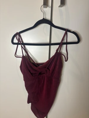 Vinröd glittrig topp - Säljer en vinröd glittrig topp från BikBok i storlek S. Klänningen har smala axelband och en snygg draperad detalj framtill. Perfekt för dig som vill sticka ut med en elegant look. Oanvänd med prislappen kvar