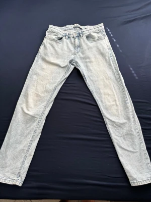 Ljusgrå raka jeans - Säljer ett par ljusgrå jeans med rak passform och klassisk femficksdesign. Jeansen har bälteshällor, dragkedjegylf och är tillverkade i ett mjukt denimtyg. Perfekta för en avslappnad och trendig look.