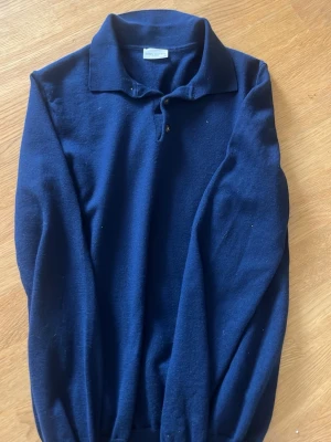 Mörkblå stickad tröja John Henric - Mörkblå stickad tröja från John Henric med klassisk krage och två knappar vid halsen. Tröjan har lång ärm och ribbade muddar vid ärmslut och nederkant. Perfekt för dig som gillar stilrena och tidlösa plagg. Sitter mer som xs