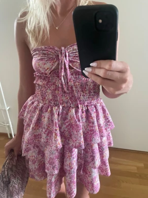 Rosa kortklänning med volang - Supersöt kort klänning i rosa med blommigt mönster. Klänningen går att knyta på olika sätt framtill, har smock upptill och volangkjol i flera lager! Jag köpte den här på Plick men den är orginellt från shein. Klänningen är storlek xxs men jag skulle säga att den även passar xs samt S! Tveka inte att höra av er om frågor eller prisförslag! 