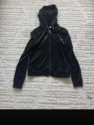 Svart velourhoodie från Gina Tricot - Mjuk och skön svart hoodie från Gina Tricot. Dragkedja framtill, två fickor och justerbar huva med breda snören. Perfekt för en chill och avslappnad stil.