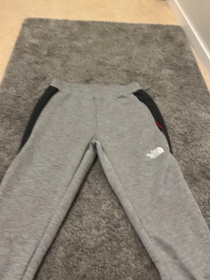 Grå mjukisbyxor The North Face säljet hela settet i min profil - Snygga grå mjukisbyxor från The North Face med svarta detaljer på sidorna och logga tryckt på benet. Byxorna har en avslappnad passform och resår i midjan. Perfekta för chill dagar eller träning. Materialet känns mjukt och bekvämt.