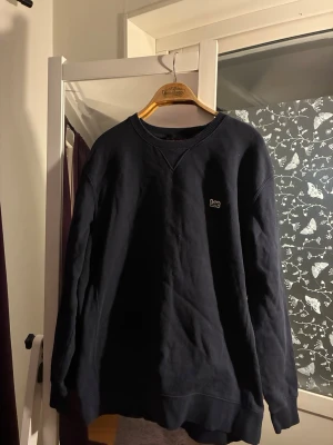 Mörkblå sweatshirt från Lee - Mörkblå sweatshirt från Lee med broderad logga på bröstet. Klassisk rund halsringning med ribbade muddar vid ärmslut och nederkant. Perfekt för en avslappnad och stilren look.