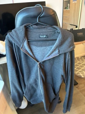 Mörkgrå zip hoodie från Black Rebel - Mörkgrå hoodie från Black Rebel med dragkedja framtill och två fickor. Klassisk modell med huva och mjukt, fleeceliknande innerfoder. Perfekt för chill dagar eller när du vill ha något bekvämt och stilrent. Enkel att matcha med jeans eller joggers.
