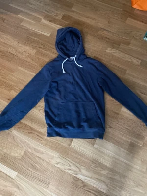 Mörkblå hoodie från Pier One - Snygg mörkblå hoodie från Pier One med klassisk känguruficka och vita dragsnören i huvan. Tillverkad i mjukt material och har långa ärmar samt ribbade muddar vid ärmslut och nederkant. Perfekt för en avslappnad stil. Tröjan är lite sliten men ingen märkbart, storleken är liten!