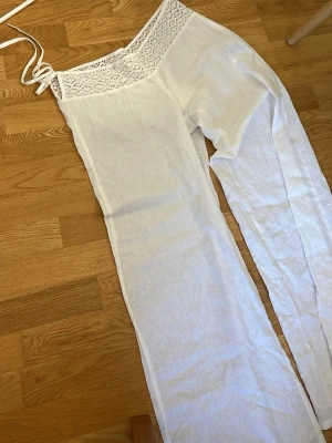 Vita linnebyxor med spetsdetaljer - Säljer ett par vita linnebyxor från Gina Tricot med snygga virkade spetsdetaljer i midjan och knytband. Byxorna har raka ben och är tillverkade i ett tunt, luftigt linnematerial som passar perfekt för varma dagar.