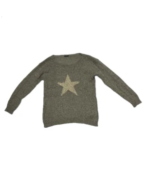 Grå/beige stickad tröja med guldig stjärna - Stickad grå/beige tröja med en guldig stjärna framtill från Motivi. Tröjan har rund halsringning, långa ärmar och ribbade muddar vid ärmslut och nederkant. Storlek M, inte overzised passform. Sista bilden är från Motivis hemsida när den fanns att köpa där.