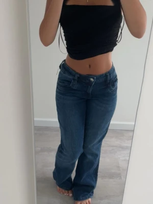 Blå utsvängda med låg midja - Säljer ett par klassiska blå jeans med rak passform och låg midja. Jeansen har fem fickor, bälteshällor och stängs med knapp och dragkedja. Perfekta till en avslappnad och trendig look. Storleken är en 164 men funkar på Xs/S. Finns en liten missfärgning vid botten av byxan, men det är inget som syns