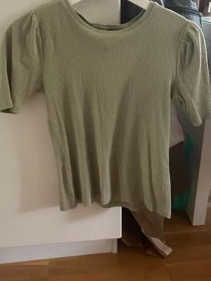 Ljusgrön ribbad topp med puffärm - Snygg ljusgrön ribbad topp med puffärm och rund hals. Toppen har korta ärmar och är tillverkad i ett mjukt, stretchigt material som sitter bekvämt. Perfekt att styla med jeans eller kjol för en trendig look.