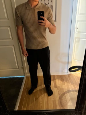 Beige ribbad polotopp | Kappahl - Säljer en beige ribbad polotopp med korta ärmar och knappar framtill. Toppen har en klassisk krage och är tillverkad i ett mjukt material som sitter snyggt på kroppen. Perfekt för en clean och stilren look.