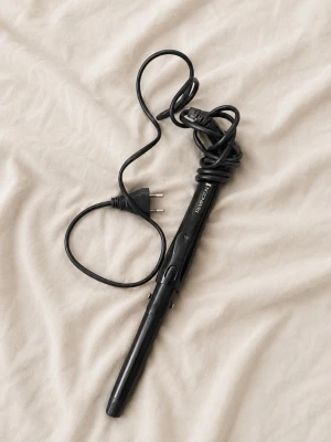 Svart locktång från Remington - En svart locktång från Remington med sladd och europeisk kontakt. Tången har ett smalt, avlångt värmeelement och ett handtag med klämma för att enkelt forma lockar. Tillverkad i plast och metall, perfekt för styling av håret.