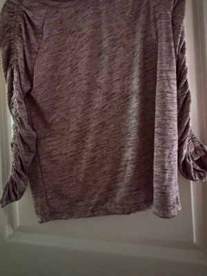 Lila  långärmad topp  - Säljer en lilamelerad  långärmad topp med snygga snörningsdetaljer längs ärmarna. Har använt den en del men fortfarande i väldigt bra skick 