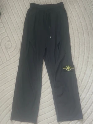 Stonę lsland  svarta byxor - Svarta nylon byxor från Stone Island med klassisk logotyp-patch på benet. Byxorna har avslappnad passform och dragsko i midjan. Perfekta för en chill och trendig look. Materialet känns mjukt och bekvämt mot huden. 