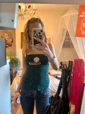 Grön Jägermeister tubtopp - Mörkgrön tubtopp med smala axelband och Jägermeister-tryck framtill. Toppen är tight och har en enkel, rak form som sitter snyggt på kroppen. Perfekt för dig som vill sticka ut med en cool och unik topp.