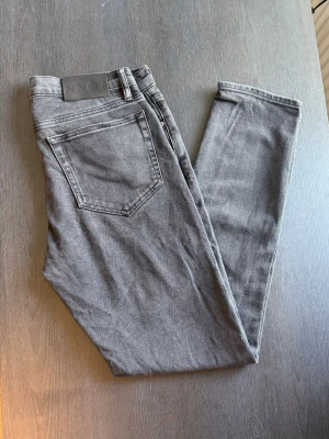 Grå slim fit jeans från NN07 - Snygga grå slim fit jeans från NN07 med klassisk femficksdesign och normalhög midja. Jeansen har en stilren look och är tillverkade i ett mjukt och stretchigt material som sitter skönt hela dagen. Perfekta för dig som gillar en modern och enkel stil.