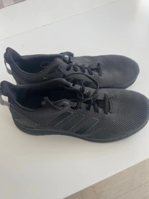Svarta  Adidas sneakers mesh - Säljer ett par svarta Adidas sneakers med klassiska tre ränder på sidan. Skorna har en luftig mesh-överdel och svarta snören. Låg modell som passar perfekt till streetwear och vardagsstil.
