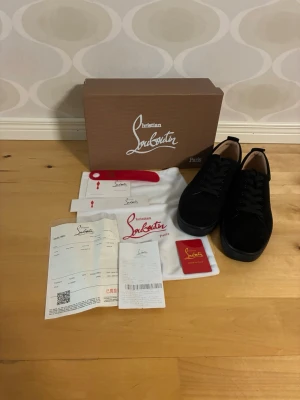 Svarta sneakers från Christian Louboutin - Stilrena svarta sneakers från Christian Louboutin i mocka med klassisk låg siluett och svarta skosnören. Skorna har diskreta detaljer och en tidlös design som passar till många olika outfits. Levereras med originalkartong, dustbag och tillbehör.