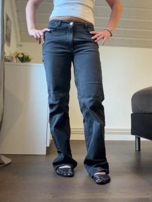 Svarta raka jeans med mid midja - Säljer ett par svarta jeans med rak passform och mid midja. Jeansen har klassisk femficksdesign, knapp- och dragkedjestängning samt raka ben. Materialet är denim i bomull. Perfekta för en avslappnad och trendig look.