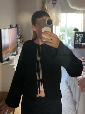 Svart knitted tie cardigan från Gina Tricot - Trendig svart kofta från Gina Tricot med knytning framtill. Koftan har långa ärmar och är tillverkad i mjukt material. Perfekt att styla över ett linne eller crop top! Jag använder inte denna längre så hoppas någon annan kan få användning av den!💕
