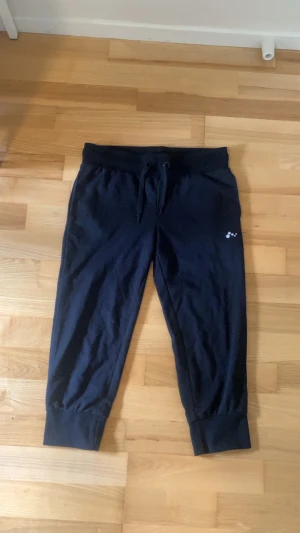 Svarta mjukisbyxor från Only Play - Svarta mjukisbyxor från Only Play med dragsko i midjan och ribbade muddar vid bensluten. Byxorna har en liten vit logga på ena benet och är tillverkade i mjukt material som känns skönt mot huden. Perfekta för chill eller träning.