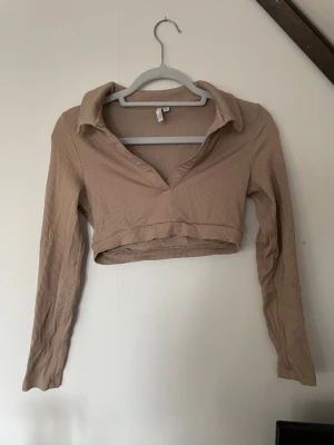 Beige croppad ribbad topp NLY Trend - Säljer en beige croppad topp från NLY Trend med lång ärm och krage. Toppen är ribbad och har en djup v-ringning.
