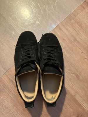 Svarta låga sneakers med rosa sula - Säljer ett par svarta sneakers med lågt skaft och snörning. Skorna har en unik rosa sula med mönster och insida i beige. Ovandelen verkar vara i mocka eller tyg och designen är enkel och stilren.