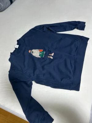 Mörkblå sweatshirt med broderad figur storlek M - marinblå collegetröja är en New Balance Athletics Sport Style Relaxed Crew med en lekfull basketgrafik på bröstet