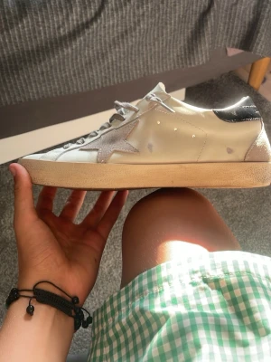GOLDEN GOOSE GGDB - Snygga vita sneakers med grå mockadetaljer och en stor stjärna på sidan. Skon har svart hälparti i läder och beige sula med vintage-look. Klassisk låg modell med vita skosnören och diskreta slitningar för en trendig känsla. Helt nya äktighetsbeviss finns allt original följer med köpta för 6000 på goolden goose små i strl passar dig som har 40 40,5 pris går o diskutera vid snabb affär