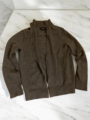 Mörkgrå stickad full zip med krage - Mjuk och stilren mörkgrå stickad tröja från riley med hel dragkedja framtill och hög krage. Tröjan har långa ärmar och ribbade muddar vid ärmslut och nederkant. Perfekt för lager på lager och enkel att matcha. Står M men har grymt så passar som XS