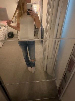Blå bootcut jeans med slitning - Säljer ett par ljusblå bootcut jeans med slitning vid knät. Jeansen har klassiska fem fickor och synliga sömmar.