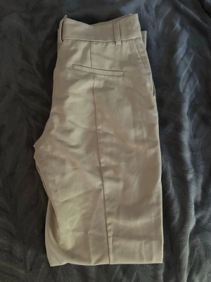 Beige kostymbyxor med raka ben - Stilrena beige kostymbyxor med raka ben och klassisk passform. Byxorna har hällor för bälte och en bakficka med diskret söm. Perfekta för en clean och snygg look.