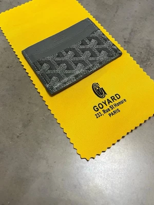 Grå kortfodral från Goy4rd - Snyggt grått kortfodral från Goy4rd med klassiskt mönster och präglad logotyp. Tillverkat i läder och canvas, perfekt för kort och sedlar. Kommer med original gul tygpåse från Goy4rd Paris.