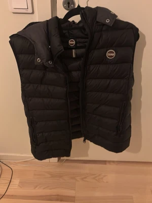 Svart dunväst från Colmar - Snygg svart dunväst från Colmar med hög krage och dragkedja framtill. Västen har två sidofickor med dragkedja och Colmar-logga på bröstet. Perfekt för lager-på-lager och håller dig varm under kyliga dagar. Nytt pris 4k.