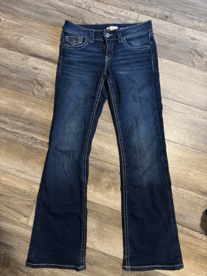 Gina tricot jeans  - Snygga mörkblå bootcut jeans med ljusa kontrastsömmar och klassisk femficksdesign. Jeansen har en liten ficka med lock och knappdetalj fram. 