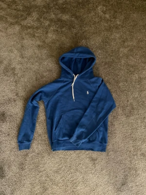 Ralph Lauren hoodie  - Snygg blå hoodie från Ralph Lauren. Liten broderad logga på bröstet och ribbade muddar vid ärmar och nederkant. Perfekt för en chill och avslappnad stil. Mjuk och skön bomullskänsla. Storlek S men passar väldigt liten som en XS eller XXS